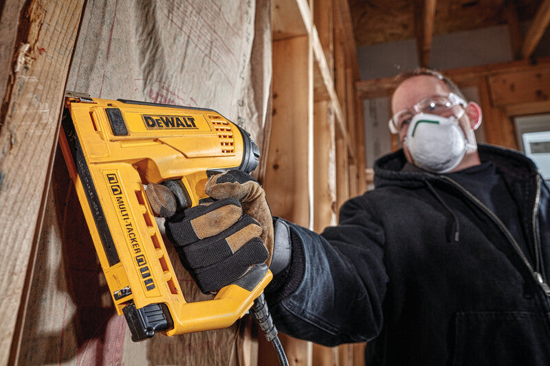 DeWalt electric staple and nail gun with integrated wire guide used in wood framing construction by worker with safety gear
