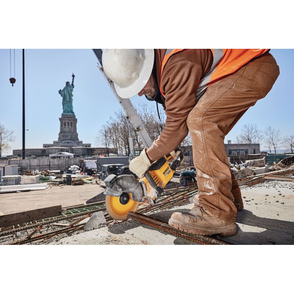 Construction worker using 9-inch Dewalt cutoff wheel to cut metal rebar on building site near Statue of Liberty