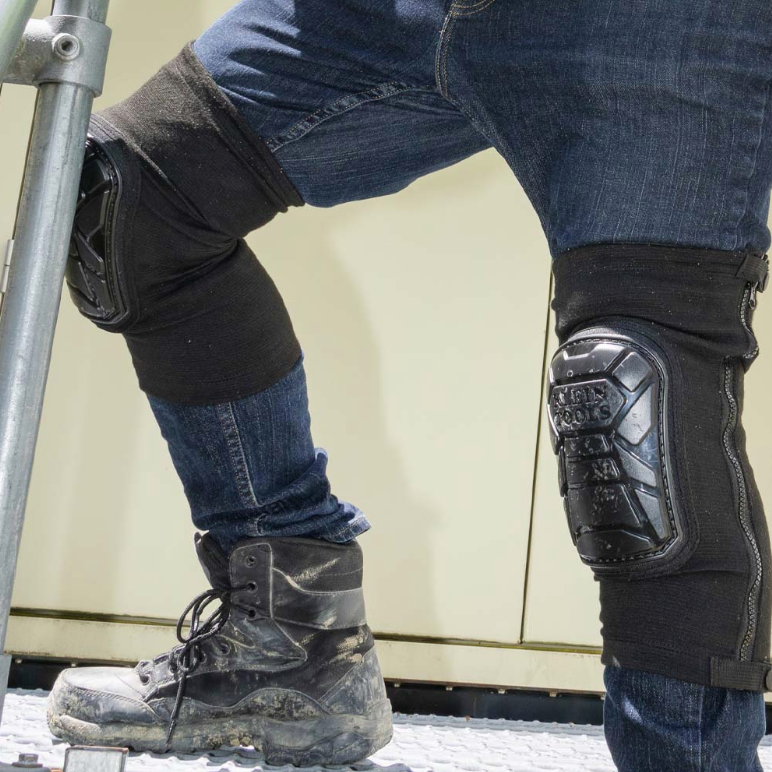 Black flexible knee pads with TPE caps, worn over jeans, designed for comfort and durability during work tasks