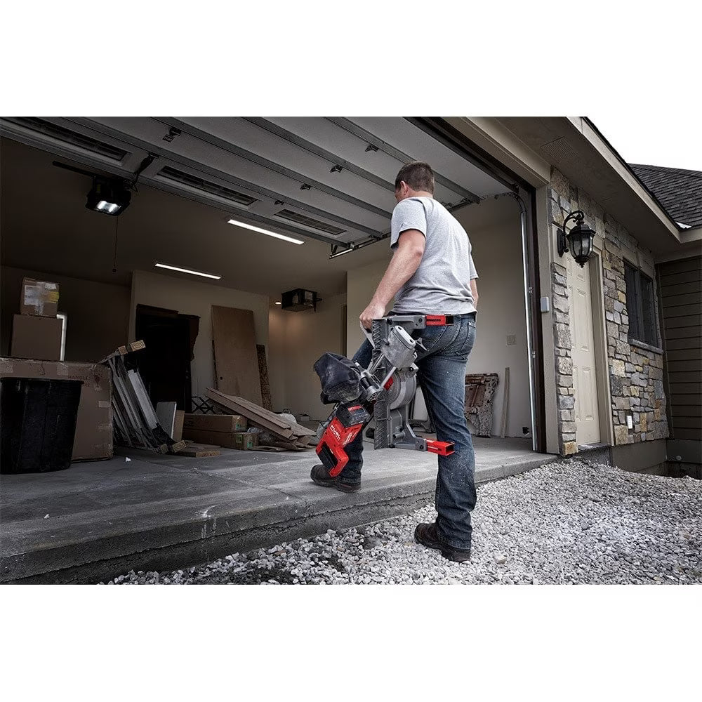 Man carrying M18 Fuel 7-1/4 inch double bevel miter saw up garage step for construction use