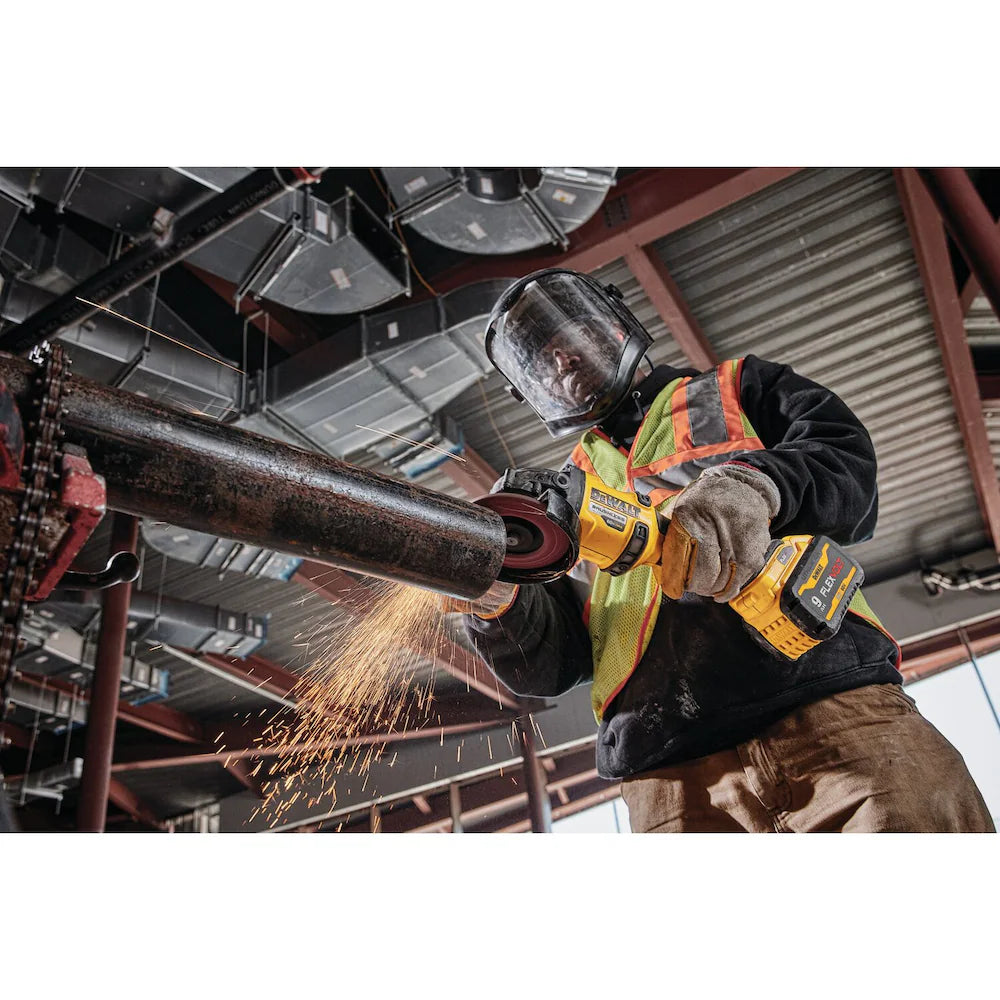 Worker using DEWALT FLEXVOLT 60V cordless angle grinder with safety gear, grinding metal pipe indoors