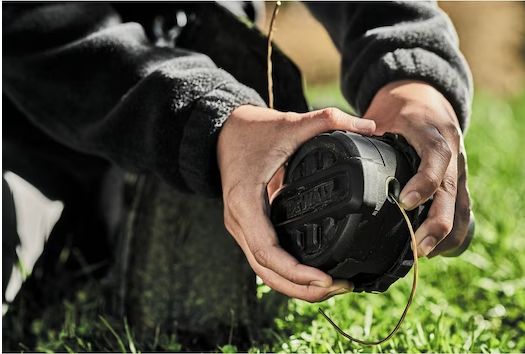 Black DEWALT QuickLoad 60V MAX trimmer spool being held outdoors for replacement or installation task